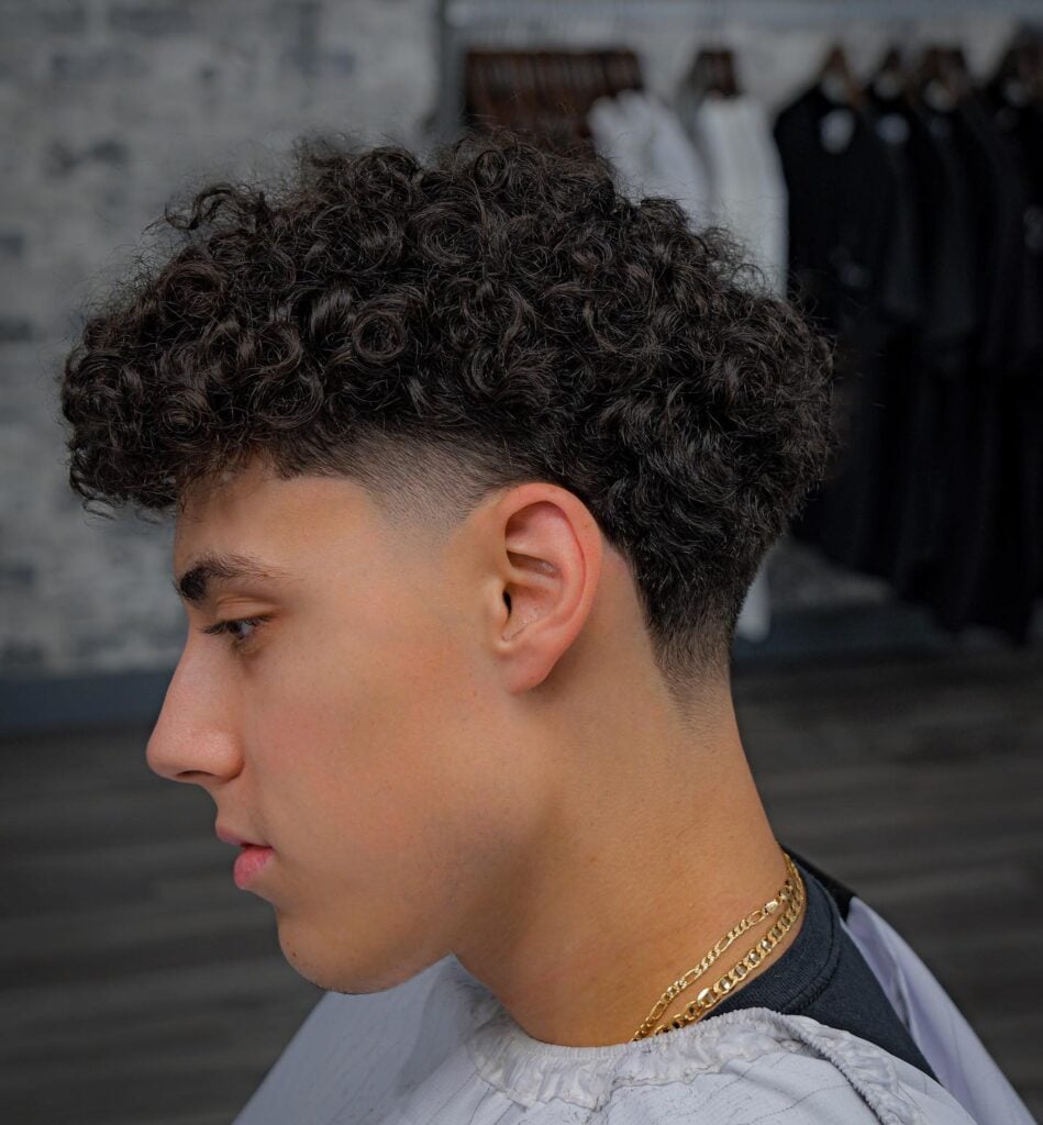 a boy with curly hair and a mid taper fade