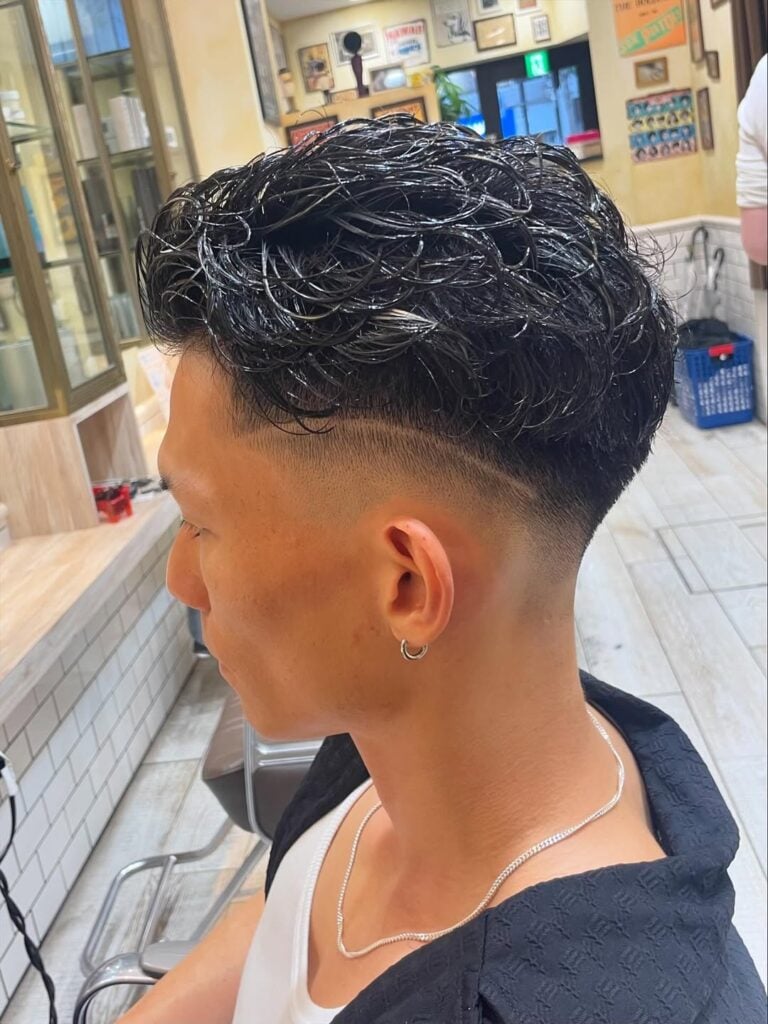 a guy at a barbershop with messy long hair on top and a fade with line
