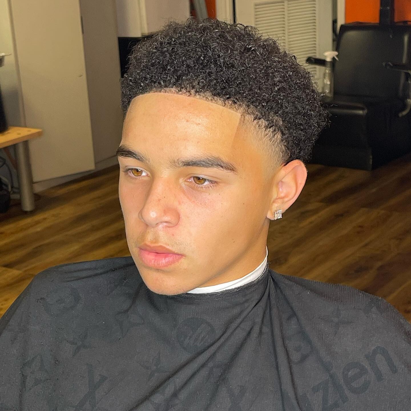 Front view of a young man with a high taper fade haircut and natural curls on top, featuring a sharp line-up and clean faded sides.