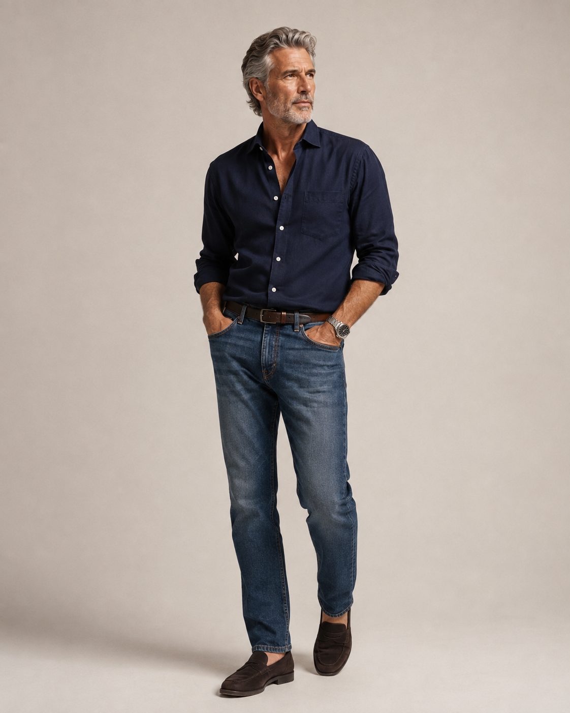Man over 50 wearing a navy shirt with straight-leg blue jeans, brown leather belt and dark loafers